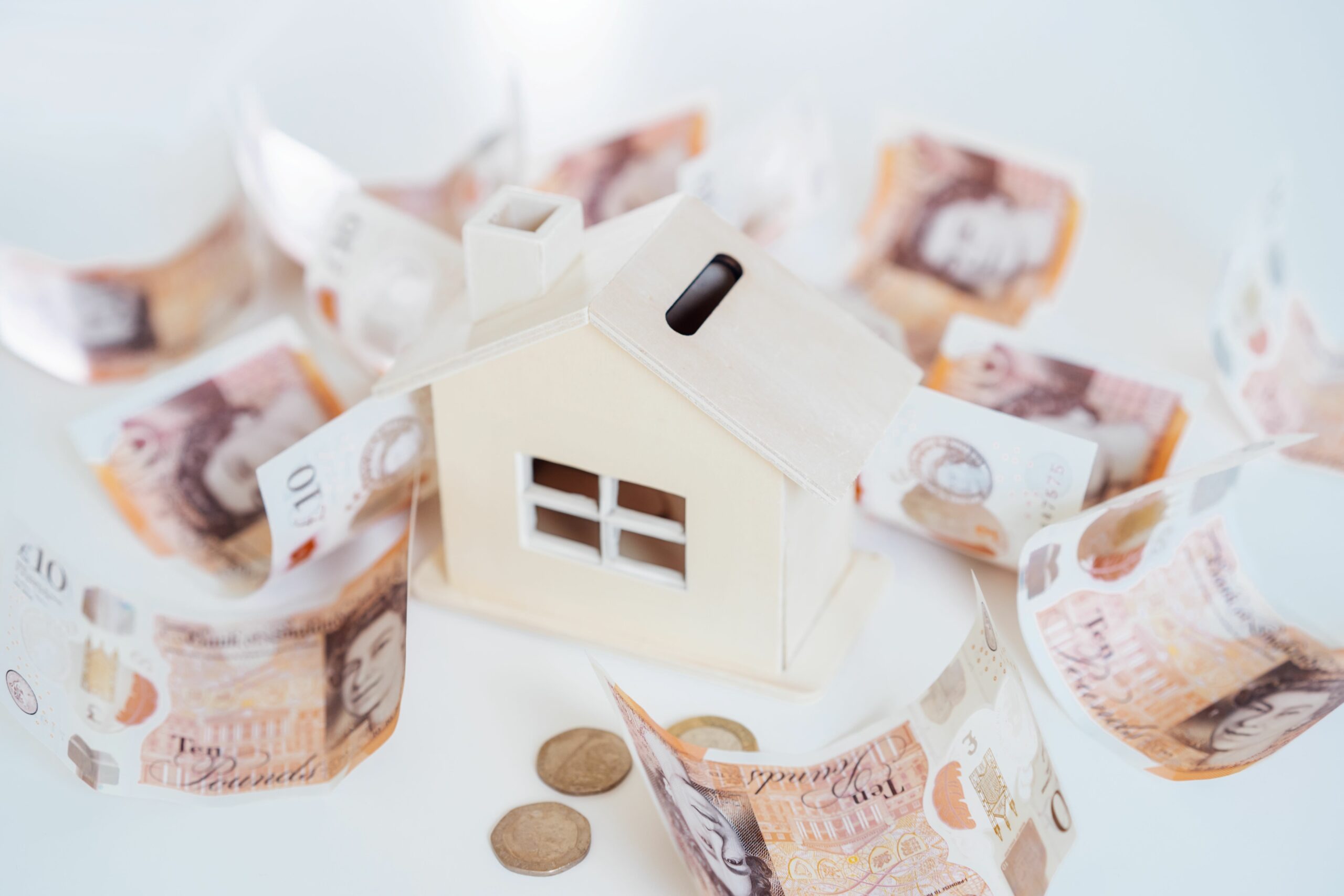 Buying a house in cash UK. Wooden House model, piggy bank with British currency on the white table.