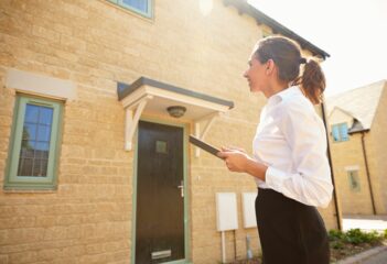 Using a home report. Female real estate agent looking at a house exterior.